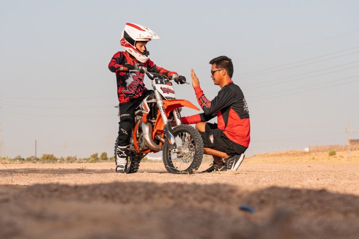 Child on a dirt bike getting a high-five from an adult on a dirt path.