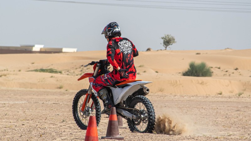 Person on dirt bike wearing red gear, riding in sandy area with cones.