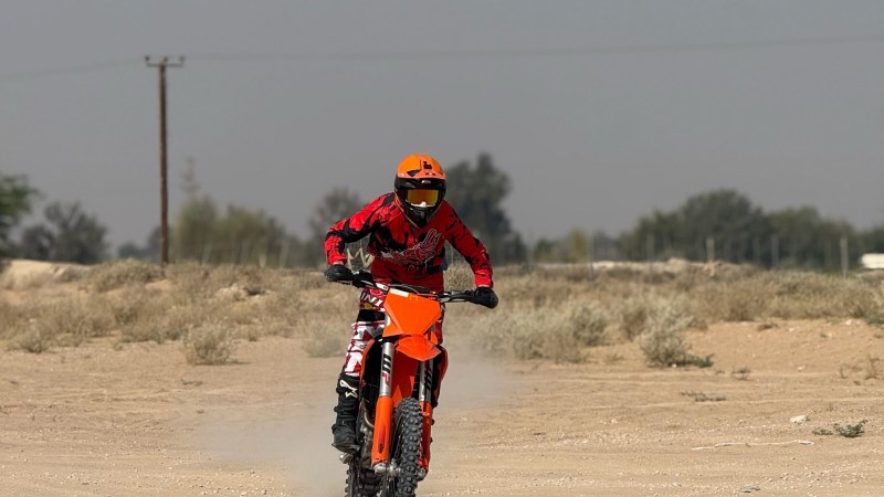 Person in red outfit riding an orange dirt bike on sandy terrain.