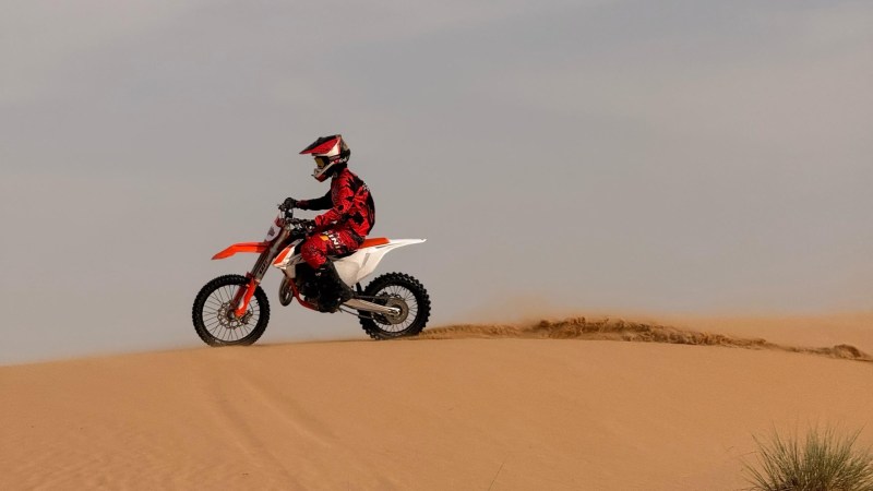 Person on a dirt bike riding over sand dunes in the desert.