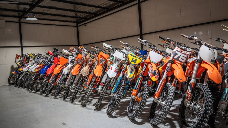Row of colorful dirt bikes lined up in a garage.