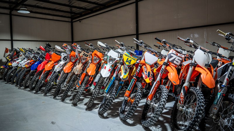 A row of colorful dirt bikes parked inside a large garage.