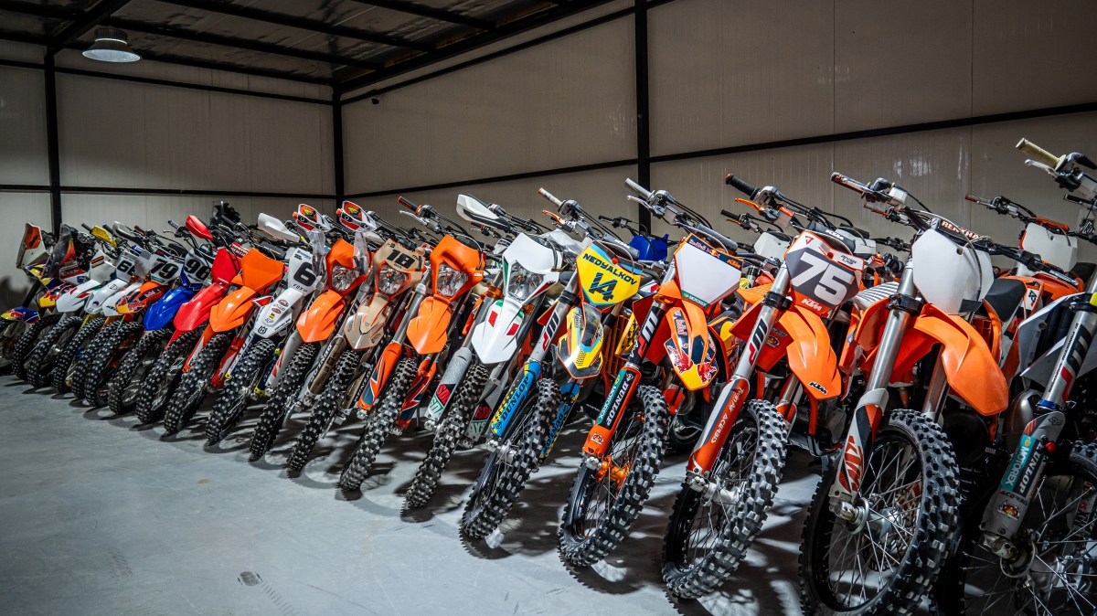 A row of colorful dirt bikes parked inside a large garage.