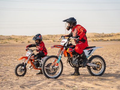 Two people on dirt bikes in desert terrain wearing protective gear.