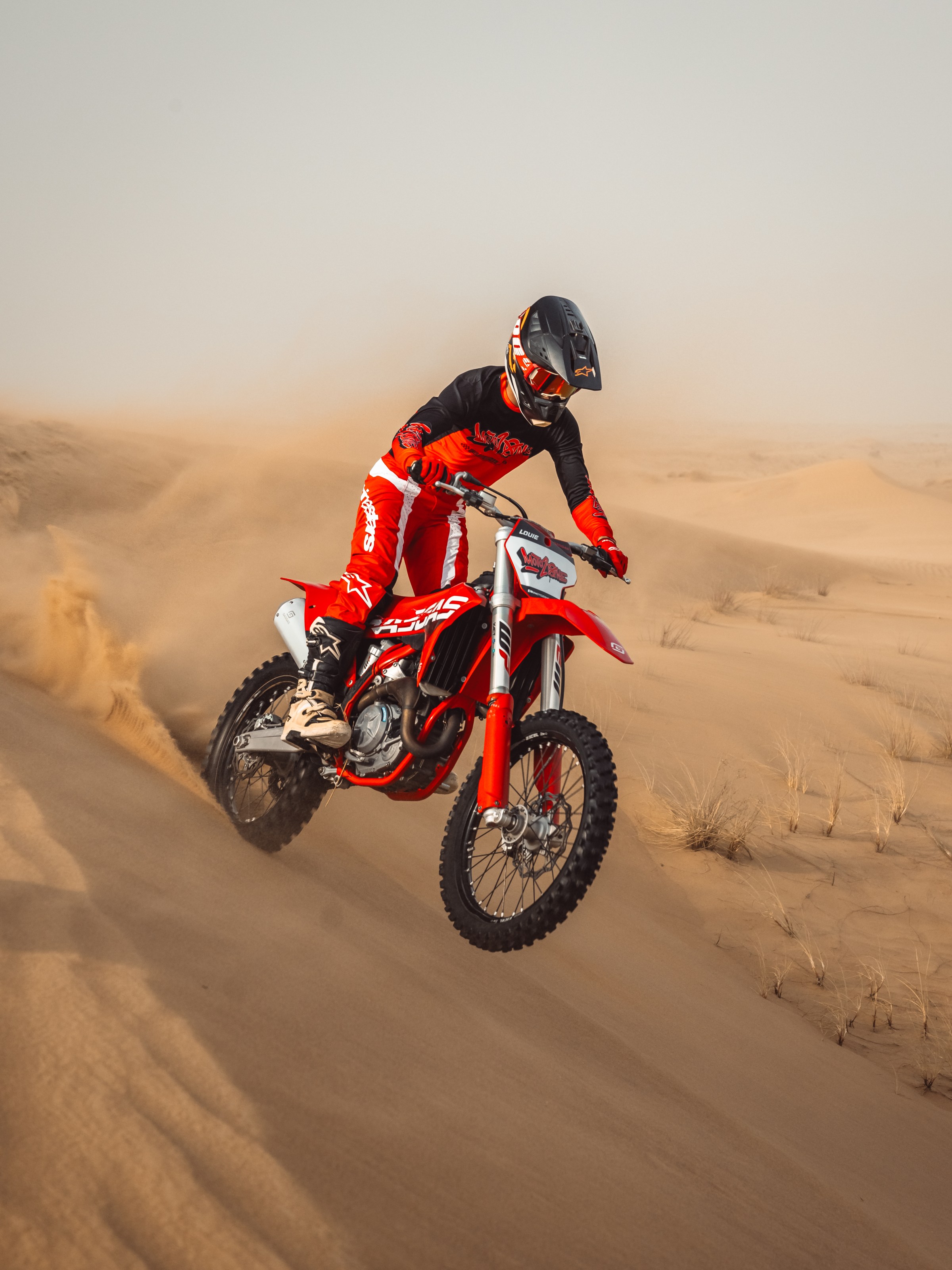 Person riding a red dirt bike through desert sand dunes.