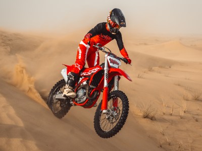 Person riding a red dirt bike through desert sand dunes.