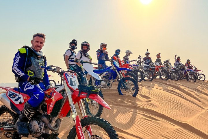 Group of dirt bikers on sand dunes under a bright sun.