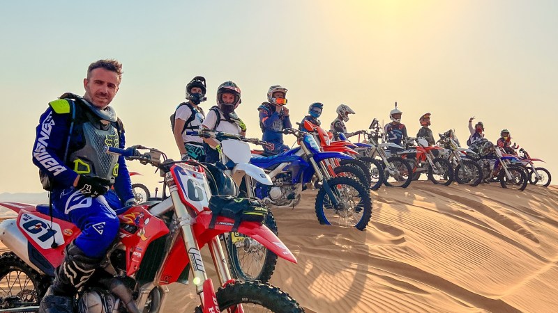 Group of dirt bikers on sand dunes under a bright sun.