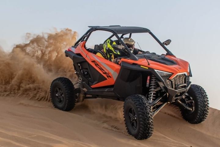 Two people driving an orange off-road vehicle on a sandy dune.