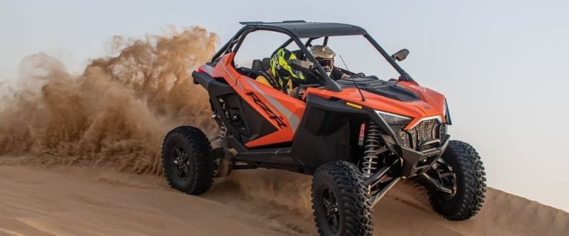 Two people driving an orange off-road vehicle on a sandy dune.