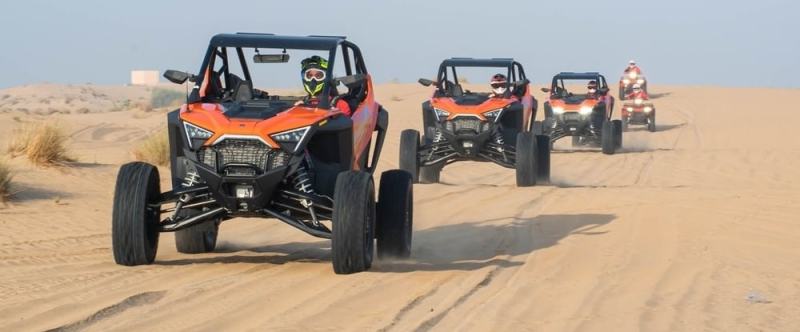 Five off-road vehicles driving in a line on sandy terrain under a clear sky.