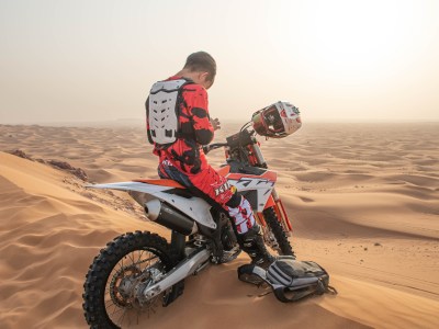 Person on a dirt bike resting on a sandy hill overlooking a desert landscape.
