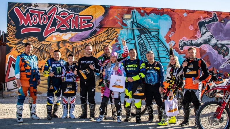 Group of motocross riders in colorful gear posing in front of a mural at MotoZone.