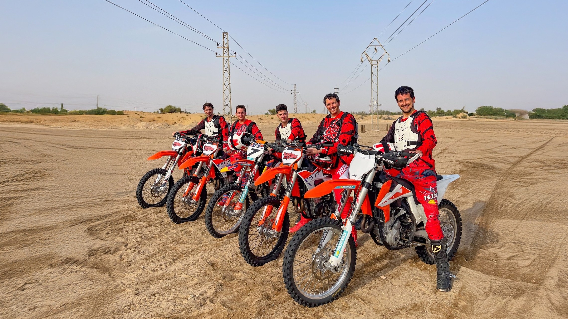 Five people in red gear on dirt bikes lined up in a desert landscape.