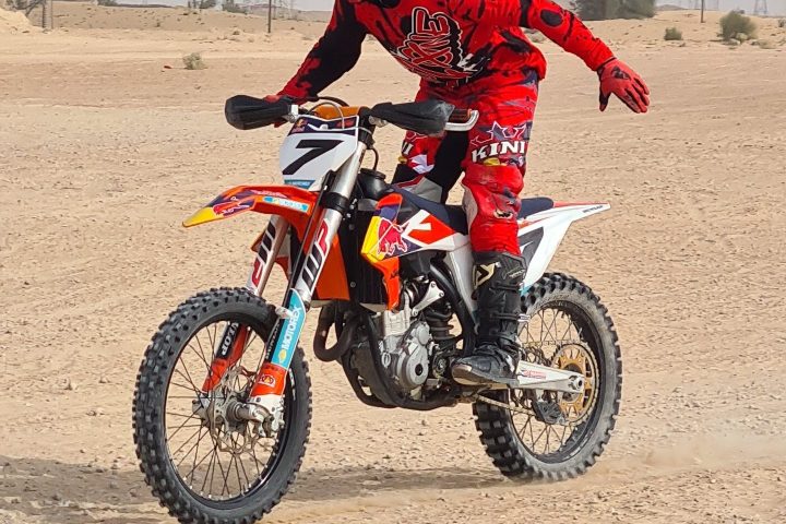 Person in red gear riding a dirt bike on a sandy terrain.
