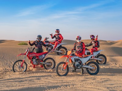 Four motocross riders in vibrant gear pose in desert dunes at sunset.
