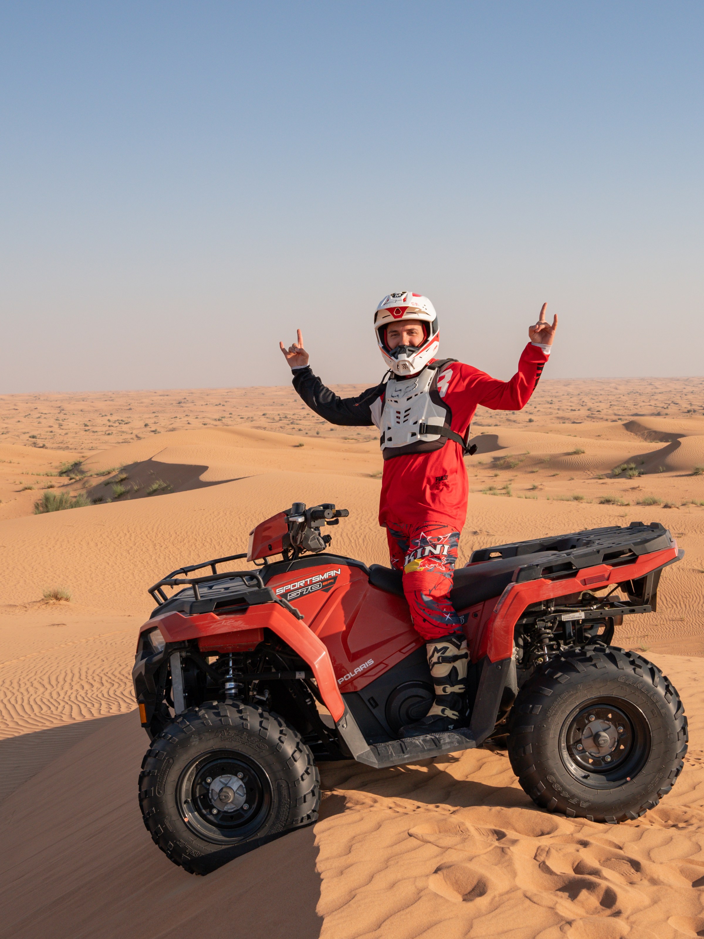 Person on a quad bike in the desert, wearing protective gear and helmet, raises arms in celebration.