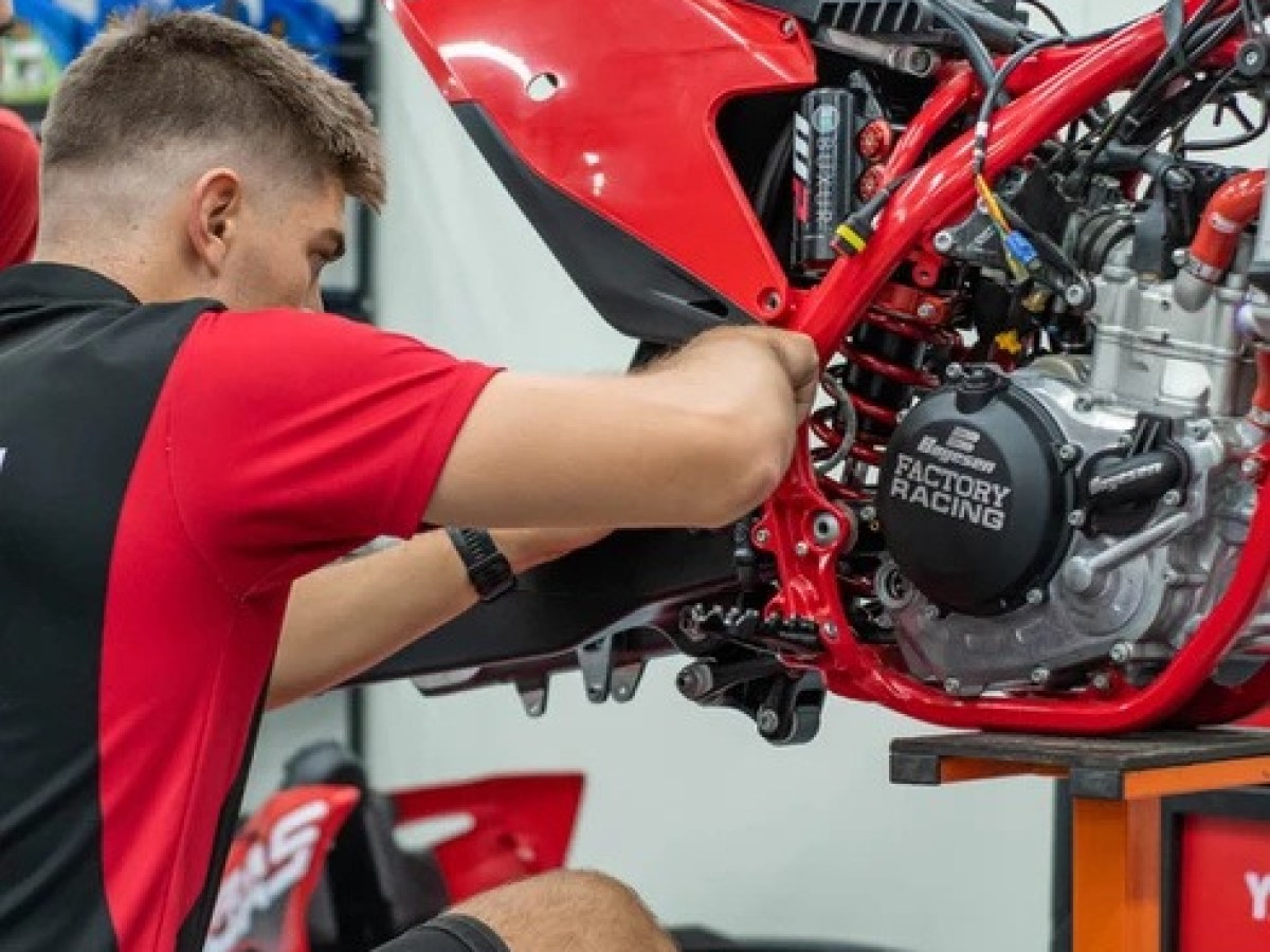 Man in black and red shirt working on a red motorcycle engine in a garage.