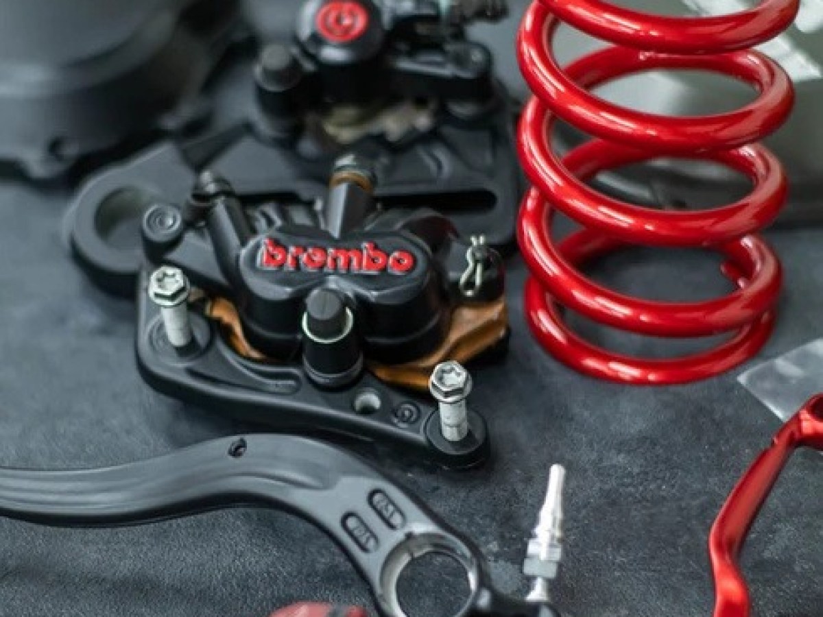 Close-up of motorcycle parts, including a red coil spring and Brembo brake components on a dark surface.
