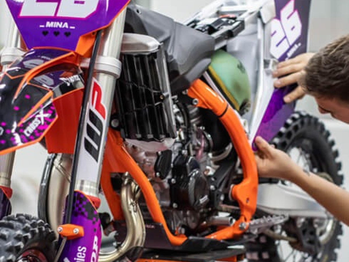 Person working on a purple and orange motocross bike with number 26 in a garage.