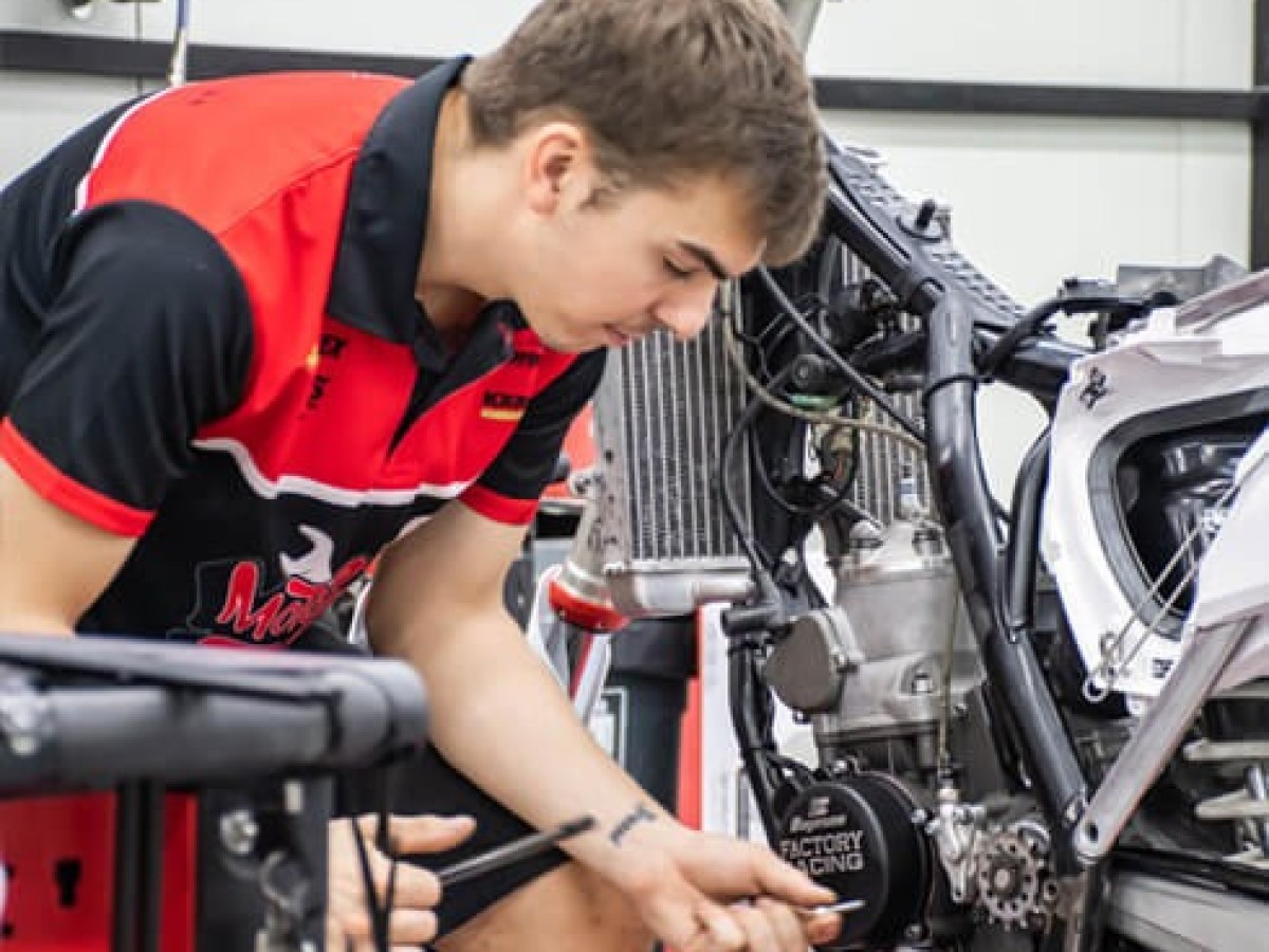 Man in red shirt repairing motorcycle in garage.