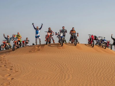 Group of motorcyclists posing with bikes on desert dune under clear sky.