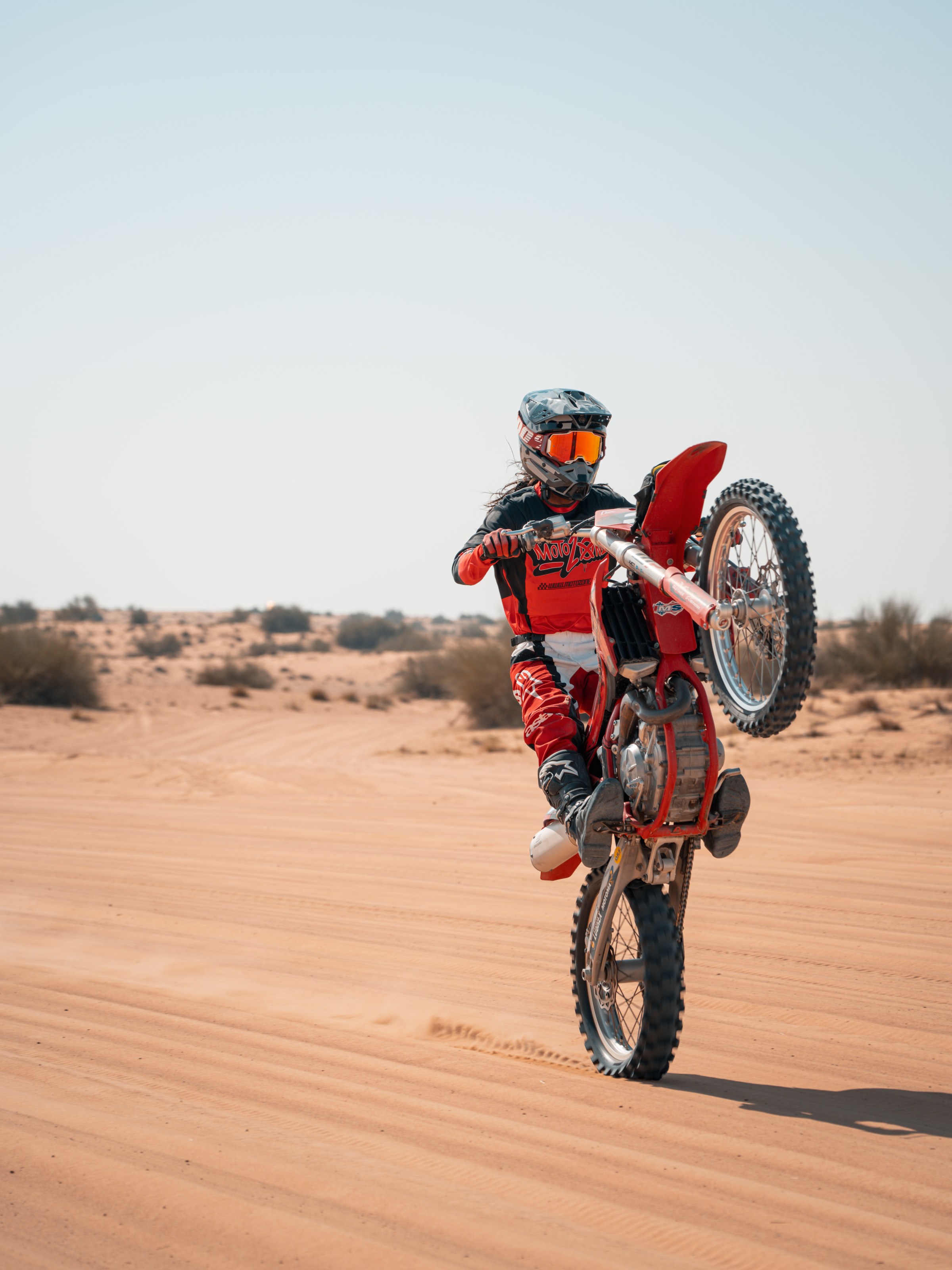 Motorcyclist performing a wheelie on a dirt bike in a desert landscape.